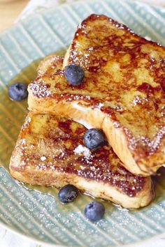 two pieces of french toast on a green plate with blueberries and powdered sugar