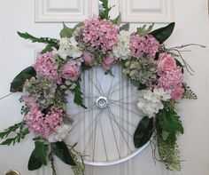 a bicycle wheel decorated with flowers and greenery on the front door to a house