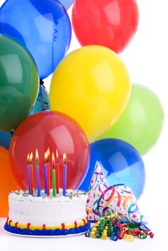 birthday cake with candles surrounded by balloons and streamers