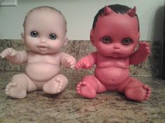 two baby dolls sitting next to each other on top of a kitchen counter, one is pink and the other is red