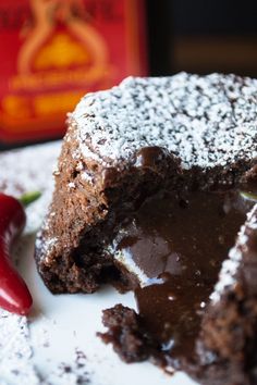 a piece of chocolate cake with powdered sugar on top and a red pepper next to it