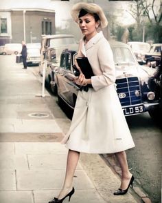 a woman in a white coat and hat is walking down the street with her book