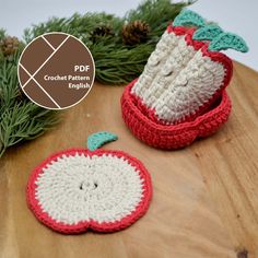 two crocheted apples sitting on top of a wooden table next to pine cones