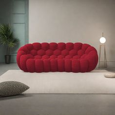 a red couch sitting on top of a white floor next to a lamp and pillow