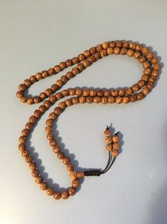 "Bodhi seed mala necklace made of 108 12mm beads with a Bodhi seed guru bead and an adjustable knot that allows you to change the length and tightness of the beads. Bodhi seeds are usually not polished so they are a solid color with small ridges or veins. Bodhi in Sanskrit translates to \"enlightened\" or \"awakened,\" therefore the Bodhi seed means \"enlightened seed.\" Bodhi is also a term in Buddhism to reflect a Buddha's understanding of the true nature of things. Many Buddhist wear the Bodh Spiritual Wooden Beaded Necklaces For Festivals, Wooden Beads Necklace For Meditation And Festivals, Wooden Beads Necklaces For Meditation And Festivals, Adjustable Spiritual Mala For Puja, Bohemian Adjustable Mala For Puja, Adjustable Traditional Mala For Healing, Spiritual Beaded Necklace With 108 Beads For Festivals, Traditional Adjustable Mala For Healing, Spiritual Beaded Necklace For Festivals