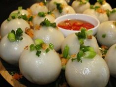 some dumplings are sitting on a plate with sauce and garnished green onions