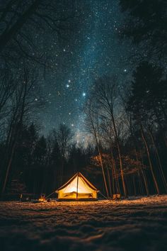 a tent is lit up in the woods at night with stars above it and snow on the ground