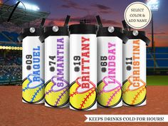 four water bottles with softballs on them in front of a baseball field