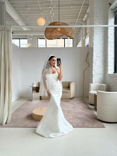 a woman in a white wedding dress taking a selfie with her cell phone while wearing a veil