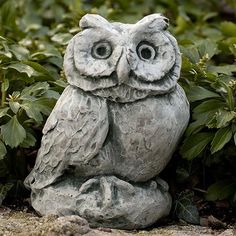 an owl statue sitting on top of a rock in front of some bushes and plants