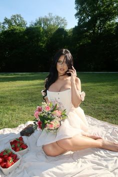 a woman in a white dress is sitting on the grass and talking on her cell phone