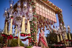 a woman in a pink sari standing under a chandelier with flowers on it