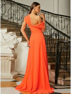 a woman in an orange dress standing next to a stair case and looking off into the distance