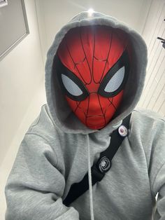 a person wearing a spider man mask and grey hoodie in a bathroom with white walls