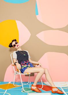 a woman sitting on top of a white chair in front of a wall with colorful shapes