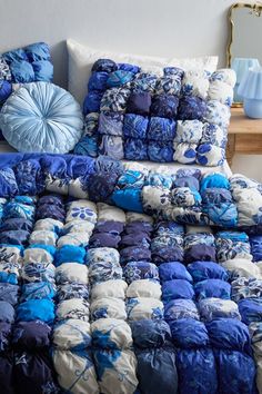 a bed with blue and white pillows on top of it next to a wooden table