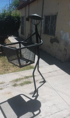 a metal object with a basket attached to it on the side of a road next to a building