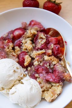 a white bowl filled with fruit and ice cream on top of a wooden table next to a spoon