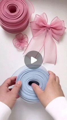 someone is holding a roll of ribbon with pink and blue ribbons next to it on a white surface