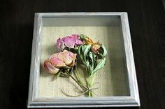 three dried flowers in a glass box on a table