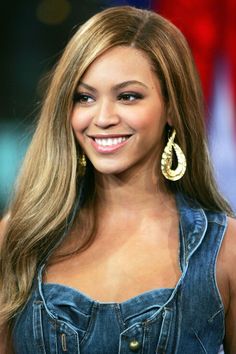 a woman with long blonde hair and large gold earrings on her face smiling at the camera