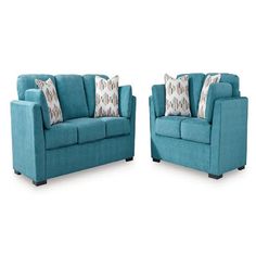 two blue couches with pillows on them sitting side by side in front of each other