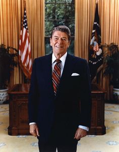 a man in a suit and tie standing in front of an american flag