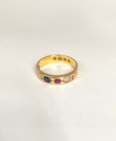 a yellow gold ring with three different colored stones on the inside and outside, sitting on a white surface