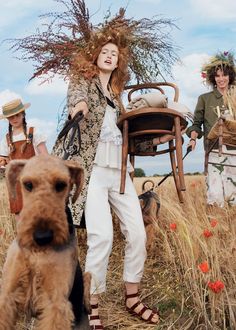 a woman standing next to a brown dog on top of a dry grass covered field