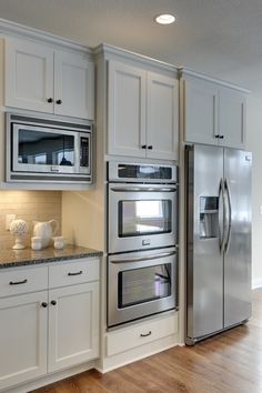 a large kitchen with white cabinets and stainless steel appliances in the center, along with hardwood flooring