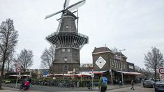 people are walking down the street in front of a windmill