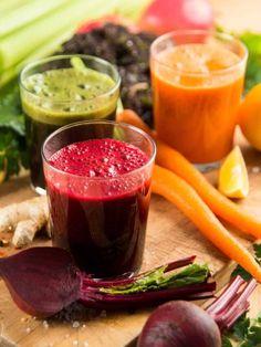 two glasses filled with liquid sitting on top of a cutting board next to vegetables and fruit