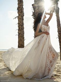 a woman in a white dress is standing on the beach with palm trees behind her