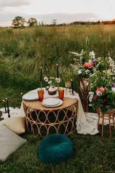 a table set up with flowers and candles in the middle of a grassy field at sunset