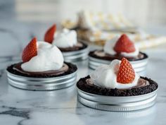 four mini chocolate desserts with whipped cream and strawberries on top, sitting on a marble countertop