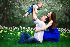 a man and woman holding a baby in their arms while sitting on the grass with daffodils behind them