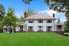 a large white house sitting in the middle of a lush green field next to trees