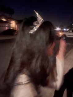 a woman taking a photo with her cell phone in the street at night, wearing a bird - like headband