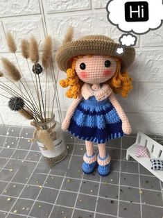 a crocheted doll wearing a blue dress and hat next to some dry grass