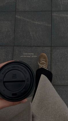 a person's feet and shoes on the ground with a coffee cup in their hand