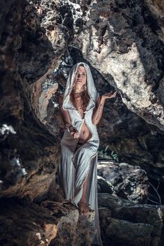 a woman in a white dress standing on rocks