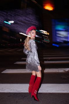 a woman standing in the middle of a cross walk wearing red boots and a sequin dress