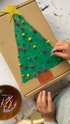 a child is painting a christmas tree on a cardboard box with colored pencils and glue