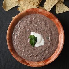 a wooden bowl filled with black bean dip surrounded by tortilla chips and sour cream