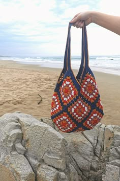 a hand holding a purse on top of a rock next to the ocean and beach