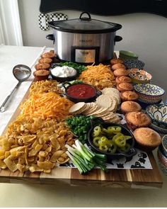 a wooden cutting board topped with different types of food next to a crock pot