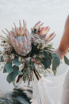 a bridal holding a bouquet of flowers in her hand on top of a beach