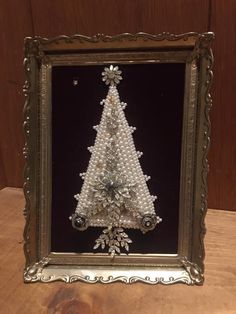 a christmas tree made out of pearls in a silver frame on a wooden table next to a wall