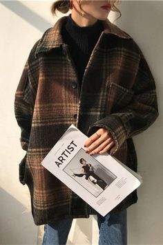 a woman standing against a wall holding a magazine