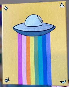 a hand holding up a painting with an alien spaceship on it's side and rainbows in the background